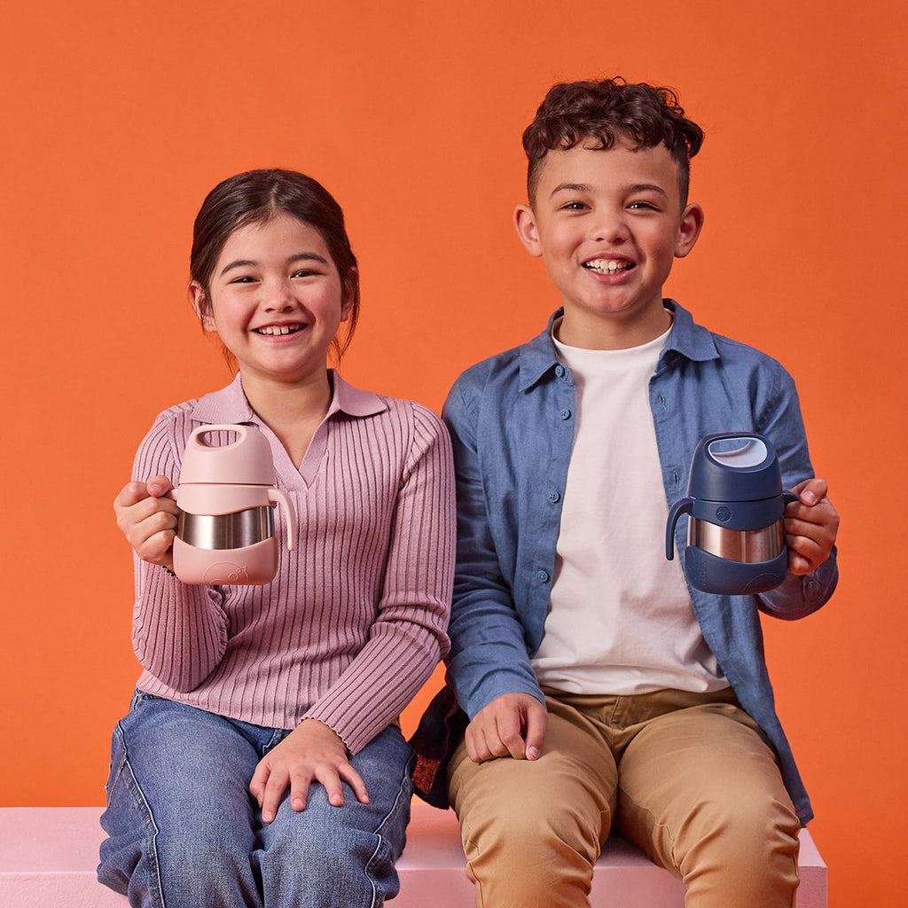 Two children holding b.box insulated food  jars against an orange background