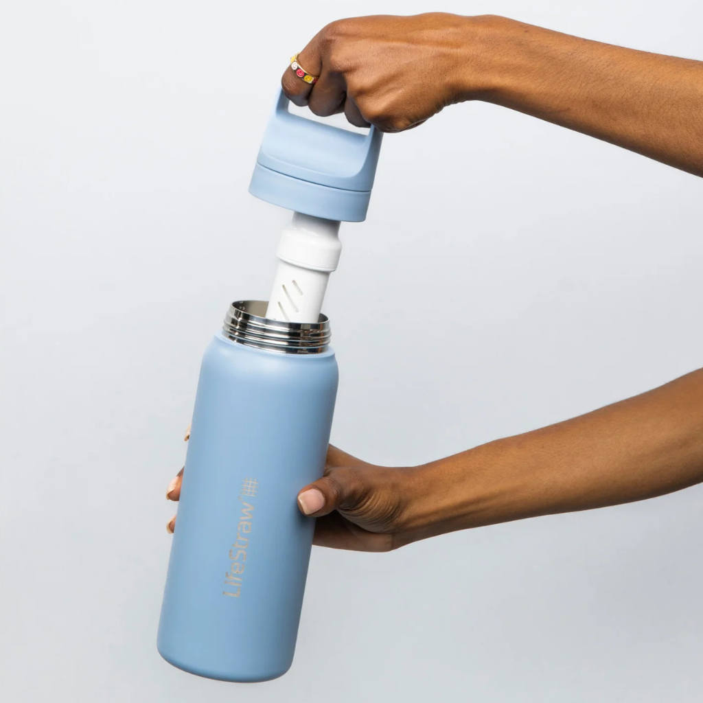 Person holding a light blue water bottle with a filter on a plain background