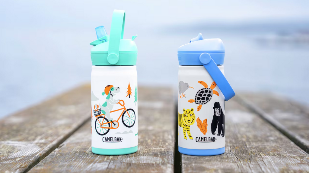 Two CamelBak water bottles with animal illustrations on a wooden surface by a body of water.