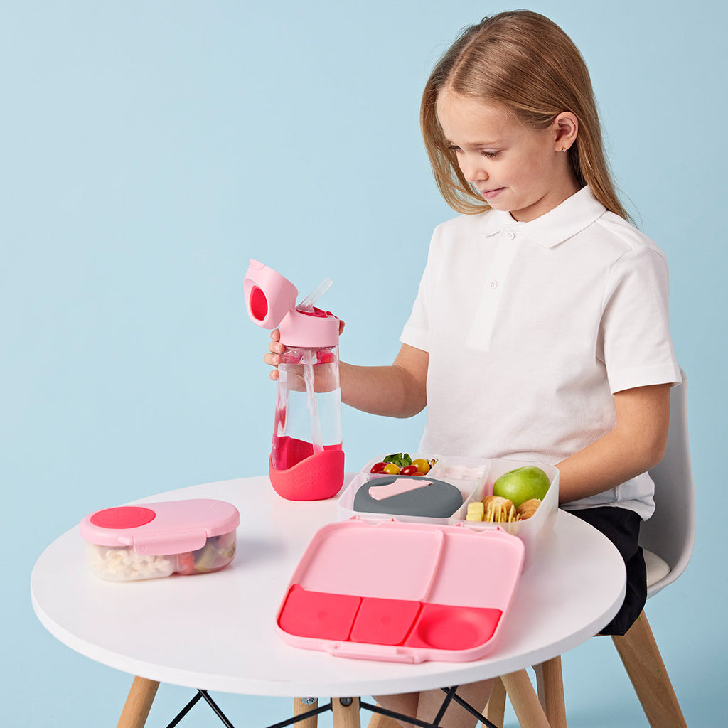 Child with pink bbox lunch box set on a table against a light blue background